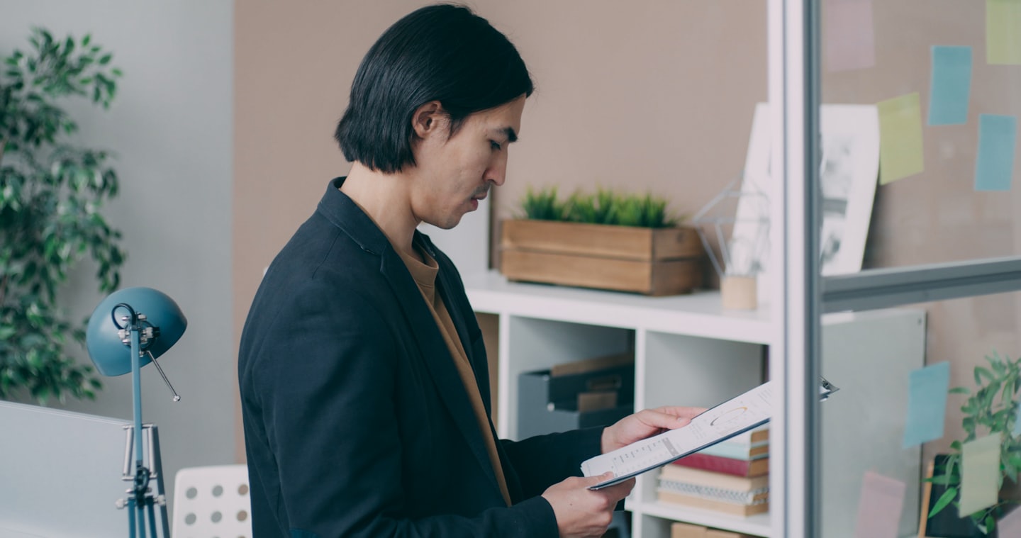 Man reviews chart in a modern office with sticky notes on glass partition.